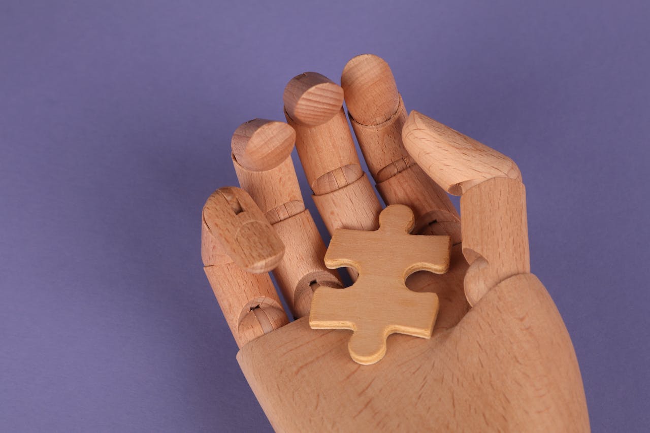 A wooden mannequin hand holds a puzzle piece against a purple backdrop.